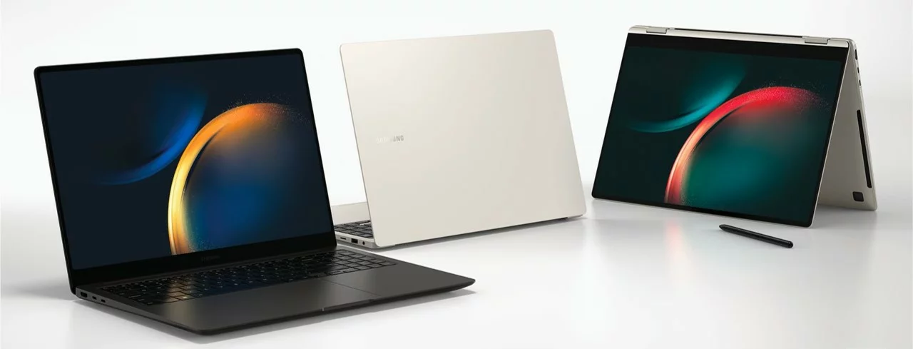 Trois ordinateurs portables sont présentés sur un fond blanc et réfléchissant. Au premier plan à gauche, un ordinateur portable noir est ouvert, affichant un fond d'écran abstrait aux couleurs vives (orange et bleu-vert). Au centre, le même modèle est vu de dos, fermé, dans une couleur crème ou blanc cassé. À droite, un modèle convertible est en mode tente, affichant le même fond d'écran coloré, avec un stylet noir posé devant lui.