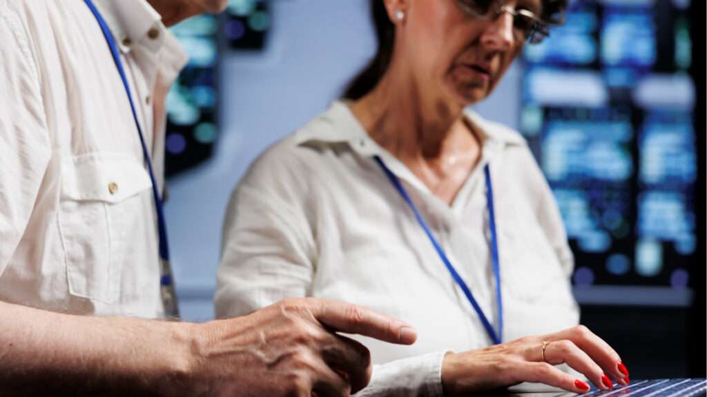 Deux personnes utilisant un ordinateur portable devant des serveurs informatiques dans une salle serveur.