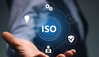 Illustration d'une main ouverte soutenant le sigle ISO, entouré d'icônes symbolisant la gestion, la qualité, la sécurité et l'innovation.