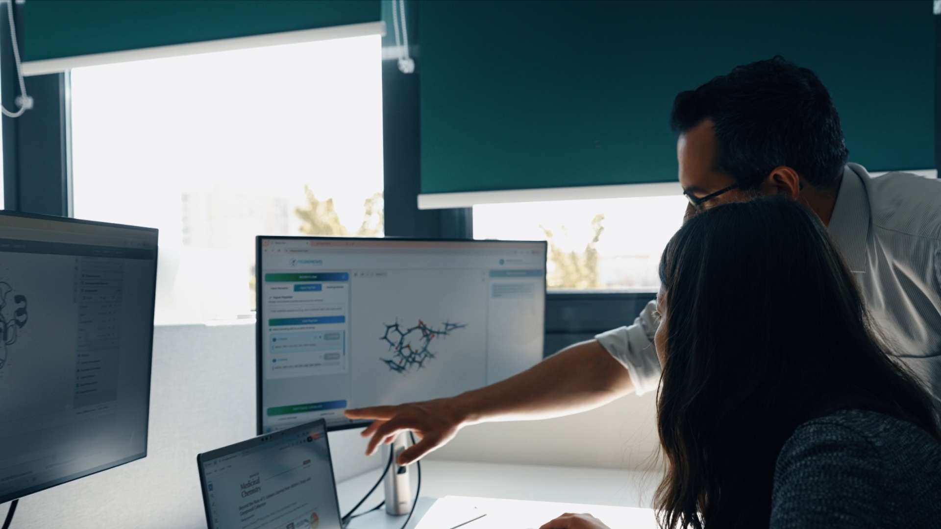 Un professionnel guide une collègue en lui montrant des données d'analyse complexes sur un écran d'ordinateur.