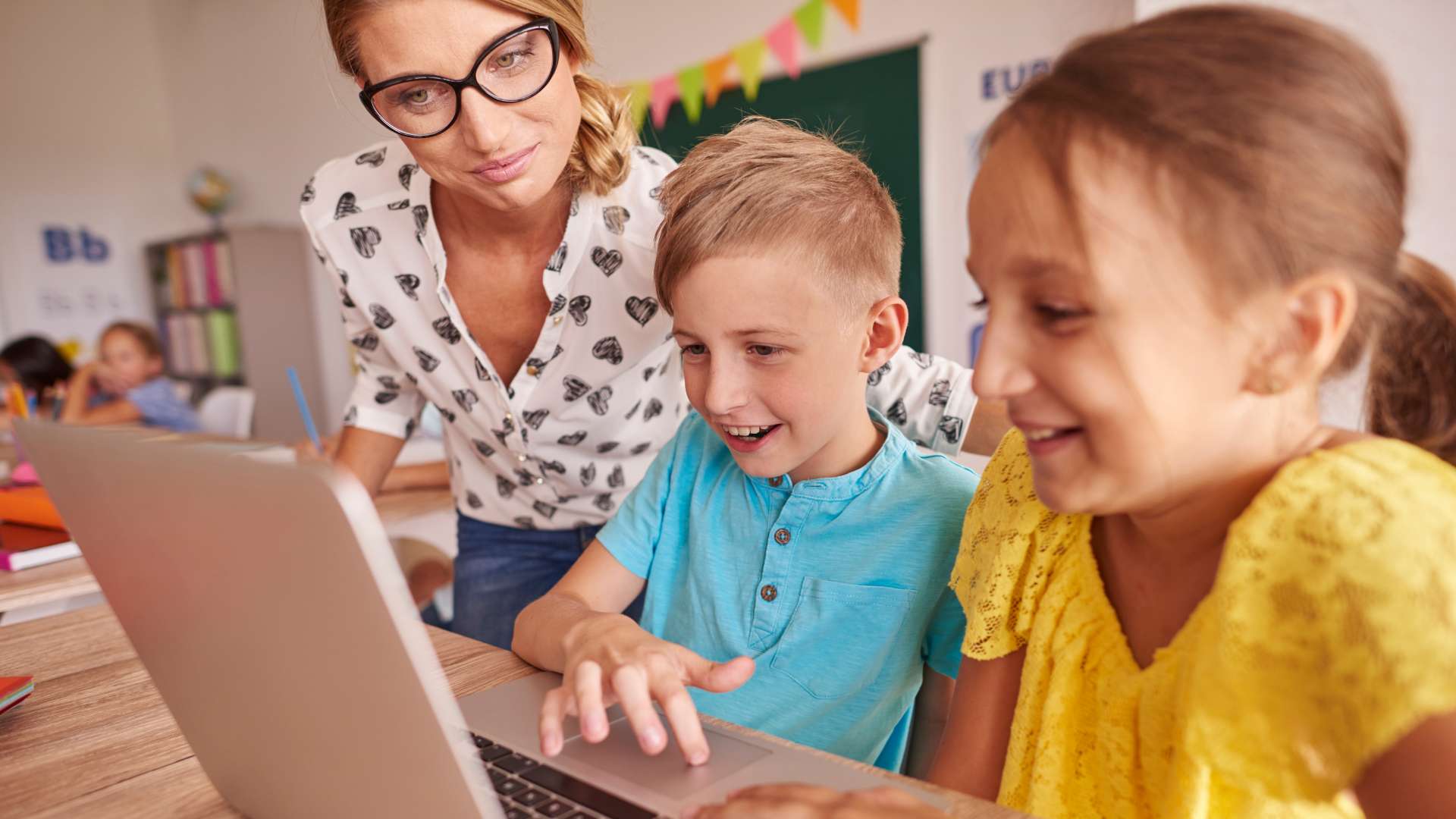 Enseignant accompagnant des enfants utilisant un ordinateur portable en classe pour un apprentissage numérique interactif