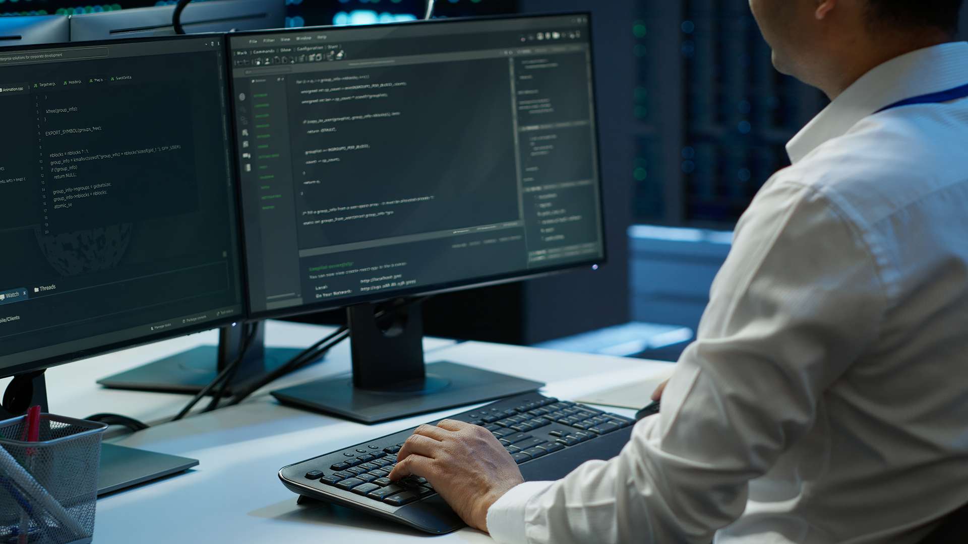 Développeur informatique travaillant sur double écran avec code et environnement de développement dans un data center moderne