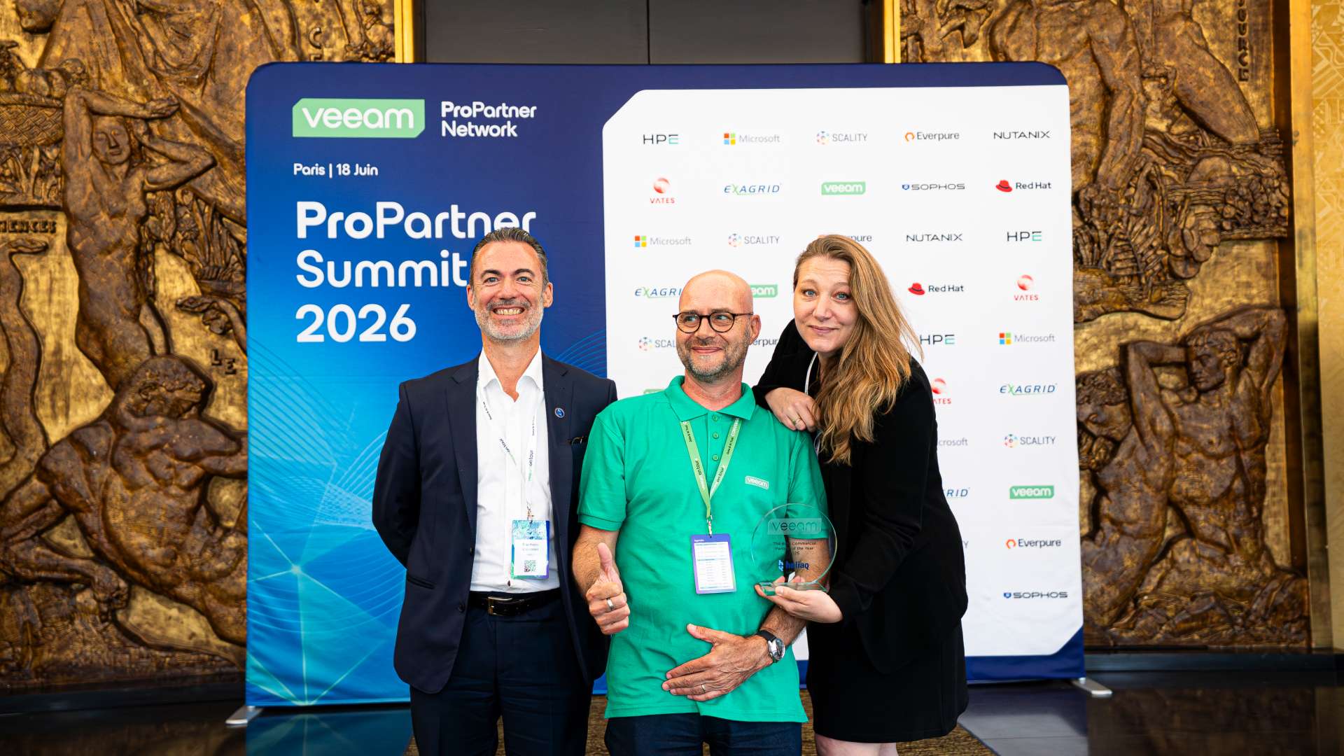 Stéphane Caumont et Maryline Flet posent devant un panneau événementiel «?Veeam ProPartner Summit 2026?» à Paris, avec logos de partenaires en arrière-plan?; l’une tient un trophée tandis que les autres se tiennent à ses côtés.