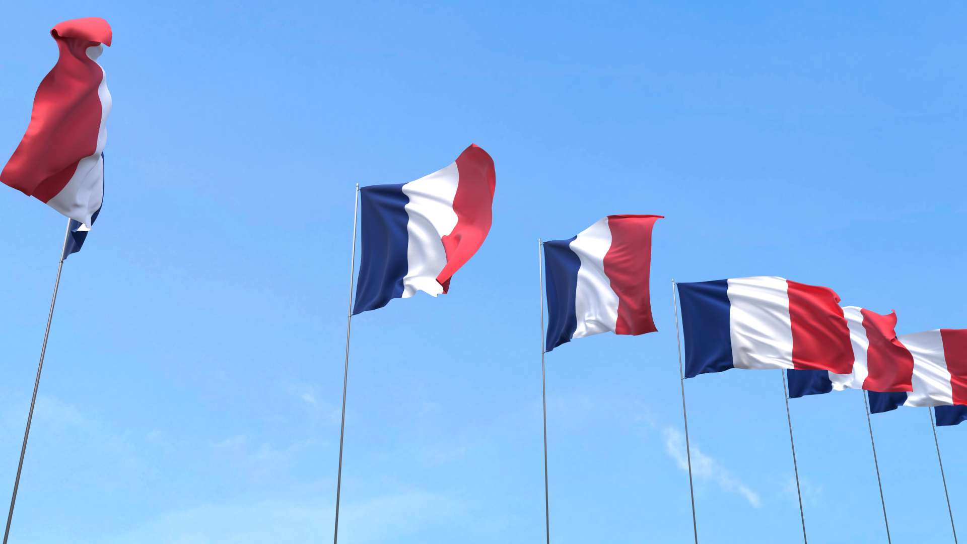 Plusieurs drapeaux français tricolores flottant au vent alignés sur fond de ciel bleu.