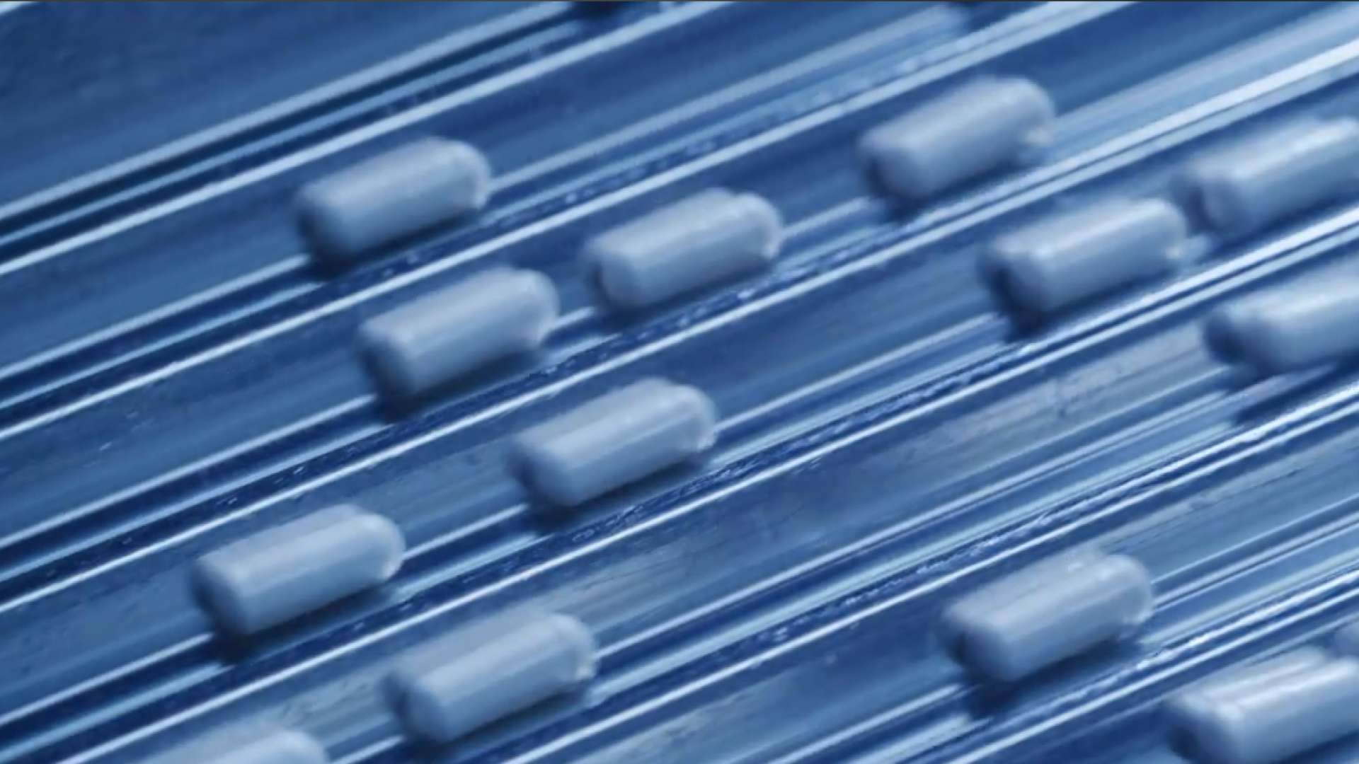 Petits éléments cylindriques blancs en relief disposés en lignes diagonales sur une surface bleue texturée.