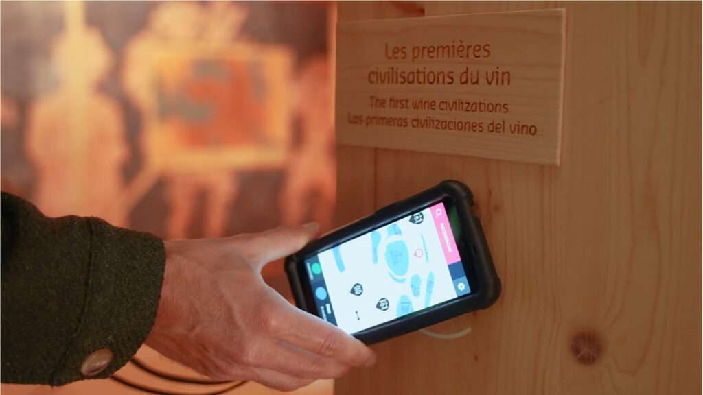 Utilisation d’un guide numérique interactif devant un panneau d’exposition sur les premières civilisations du vin.