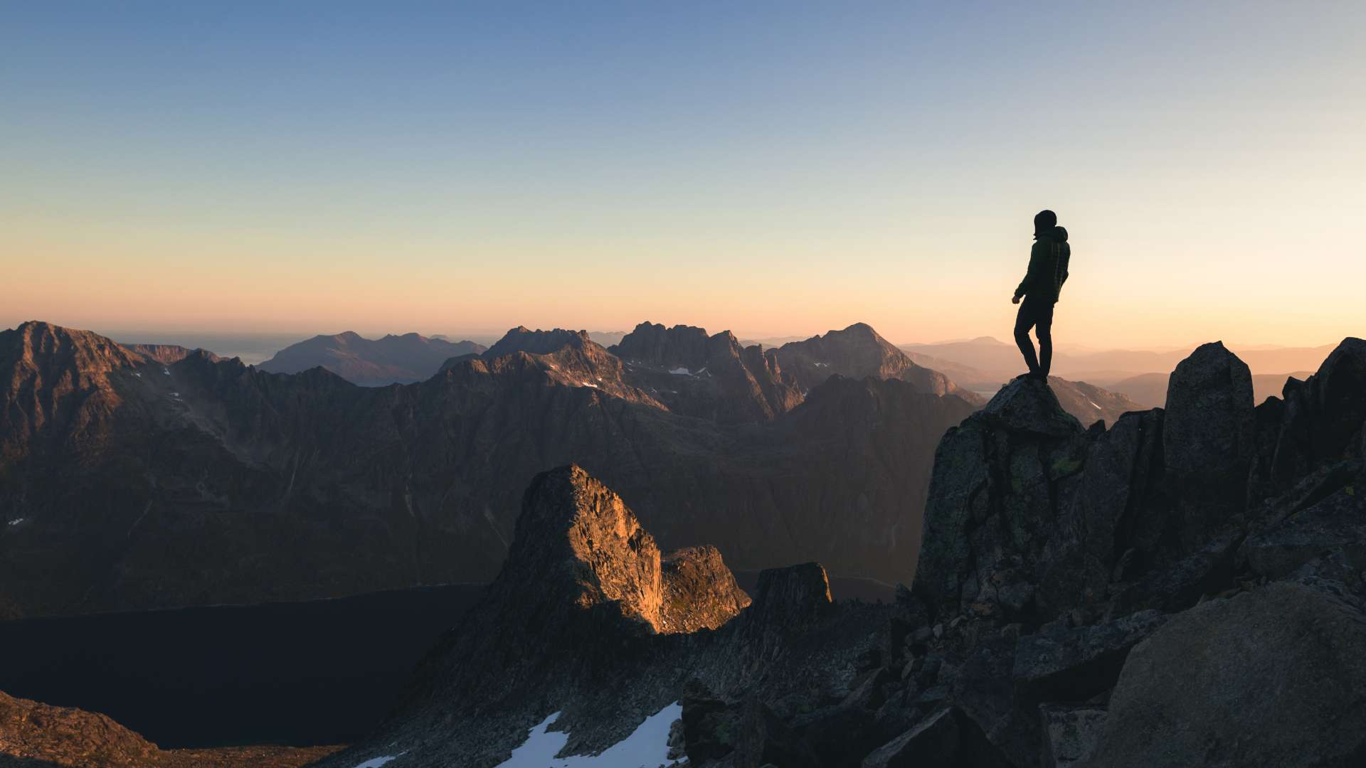 Personne sur un sommet rocheux contemplant une chaîne de montagnes au lever ou coucher du soleil.